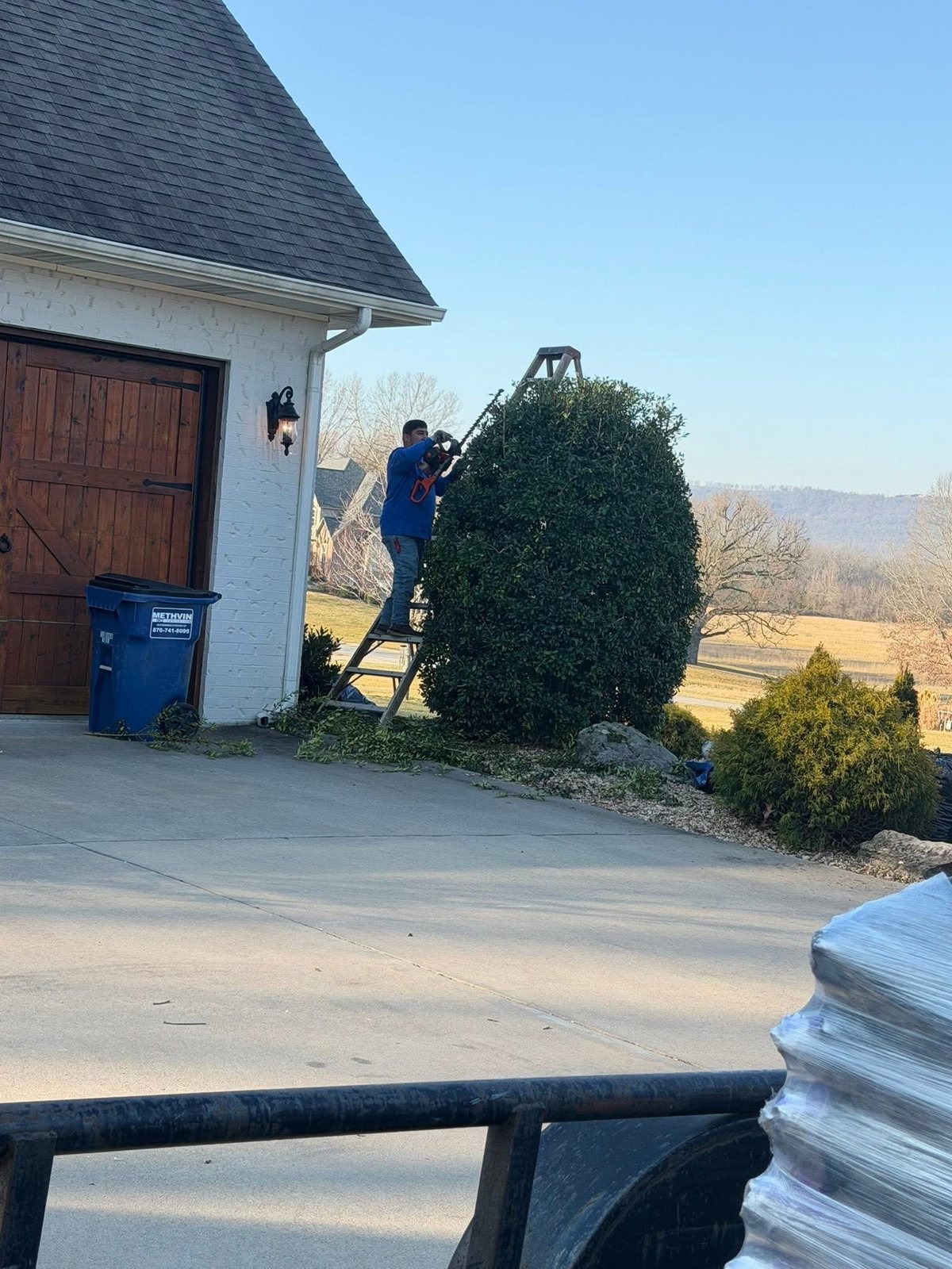 Worker on a ladder clearing the roofline above a garage door